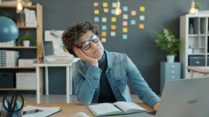 Efecto 4 PM: mujer en el trabajo quedándose dormida sobre el escritorio, símbolo del cansancio laboral y el agotamiento causado por el bache circadiano de la tarde, que afecta la energía, la concentración y la productividad en la oficina.